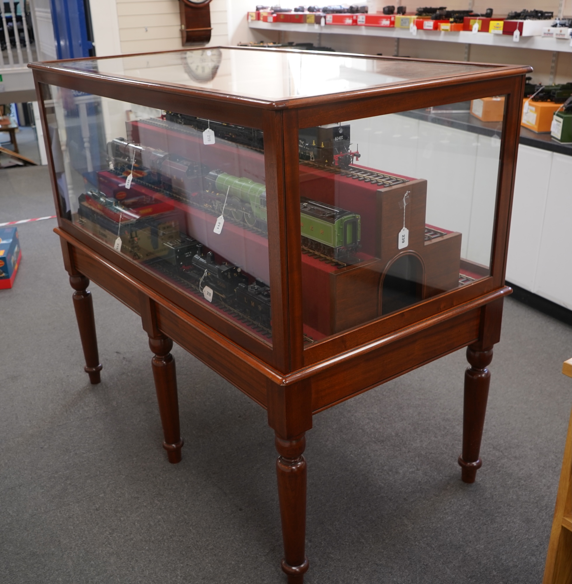 A substantial tiered display cabinet in a mahogany-tinted hardwood, with a lift off glazed cover, intended for Gauge One model railway rolling stock, currently fitted with five lengths of 45mm display railway track, dime